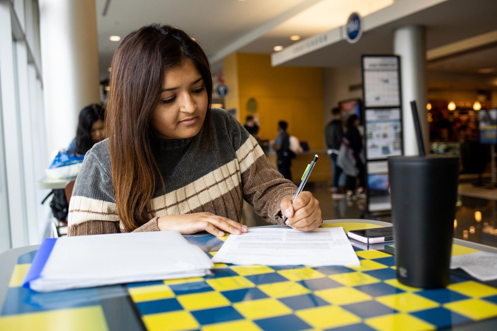 student sits at table taking notes in a tablet